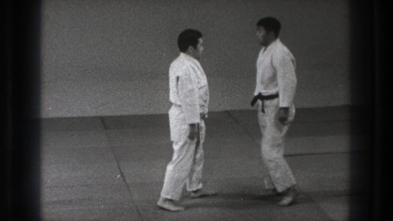 In the 1971 Tokyo dojo footage, a black-belt practitioner faces another man in a white gi on the training mat.