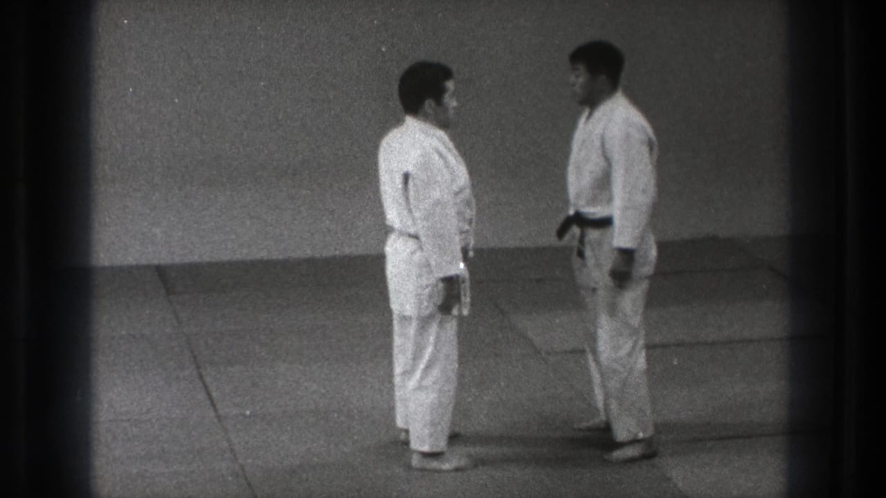 Two adult men in white gi stand at close range on the mat during the 1971 Tokyo karate training scene.
