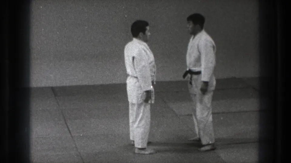 Two adult men in white gi stand at close range on the mat during the 1971 Tokyo karate training scene.