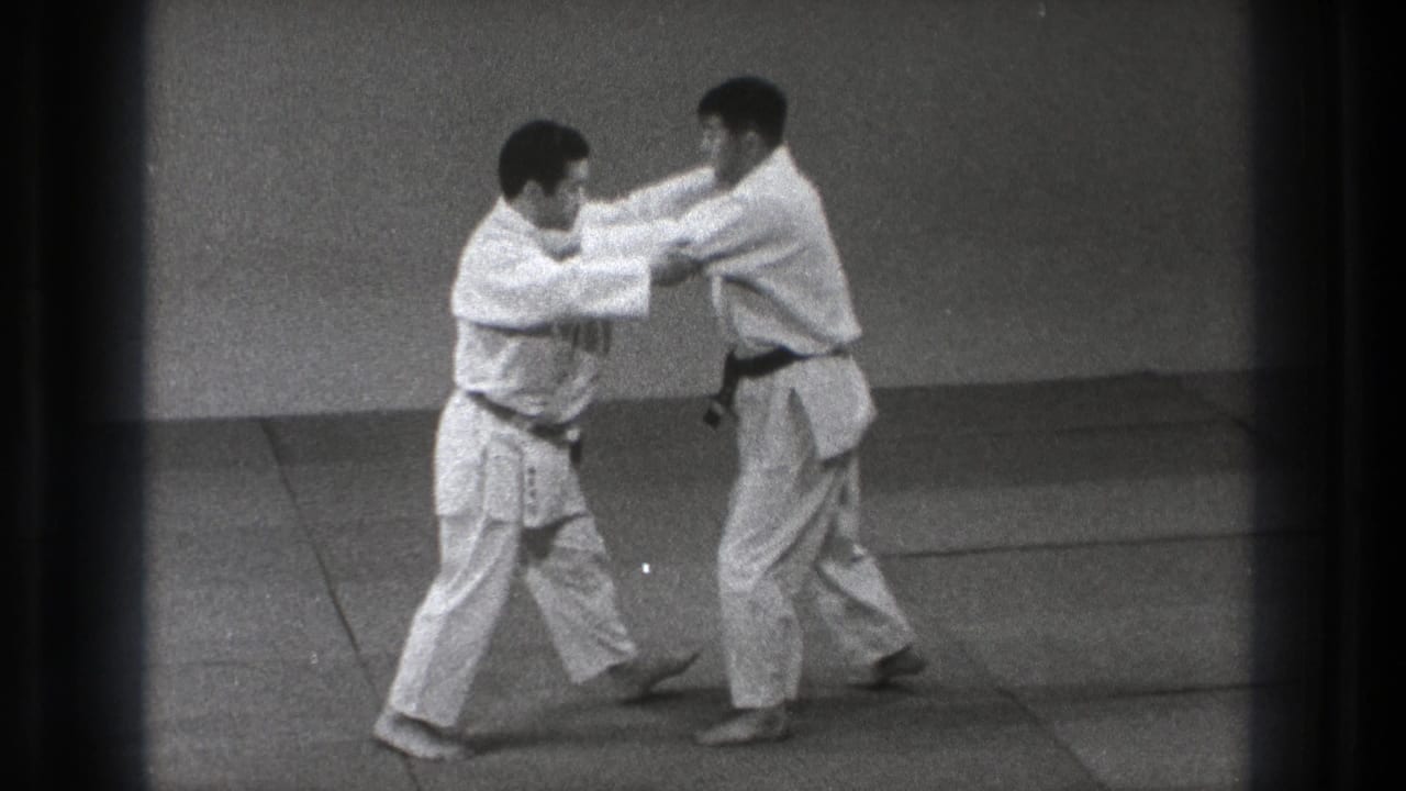 Two men in white gi grip each other on a dojo mat.