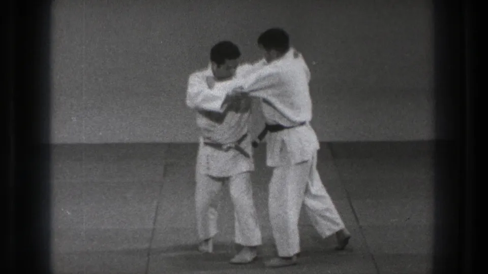 A practitioner turns inward during a paired martial arts movement as the other man stays in close contact.