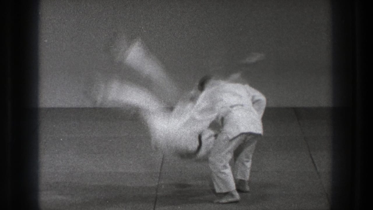 In Tokyo 1971 training footage, one martial artist in a white gi throws another across a plain mat.