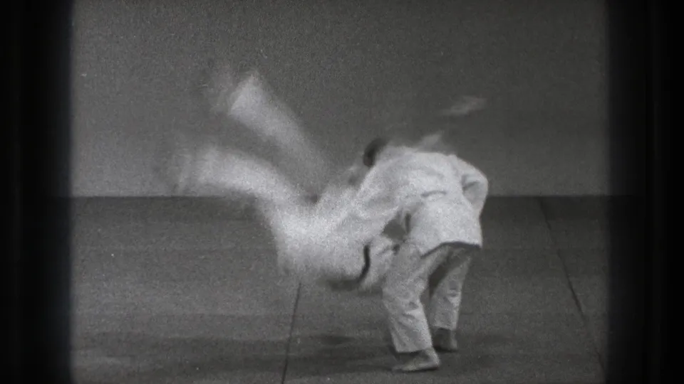 In Tokyo 1971 training footage, one martial artist in a white gi throws another across a plain mat.