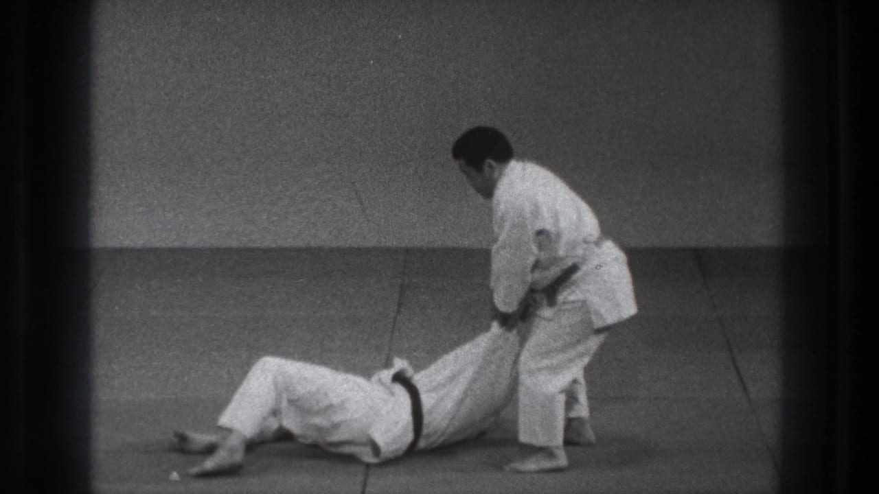 A martial artist stands over his grounded training partner after a throw in the Tokyo dojo footage.