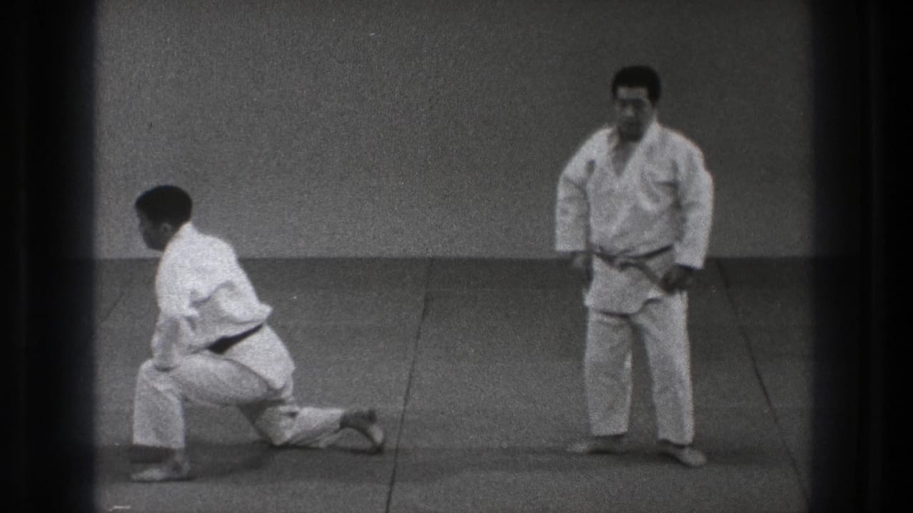 Both martial artists reset after the throw, with one kneeling and the other standing in the Tokyo training space.