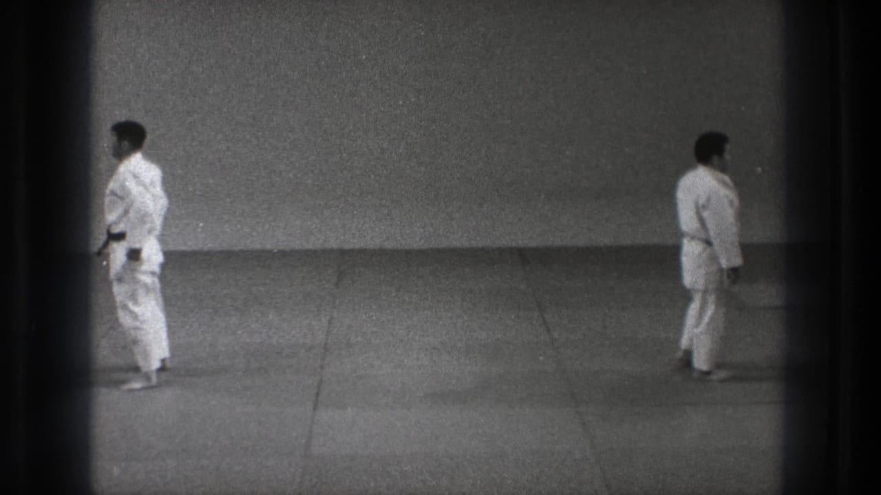 A Tokyo 1971 8mm frame shows one uniformed man near the left edge and another crossing the grey dojo mat.