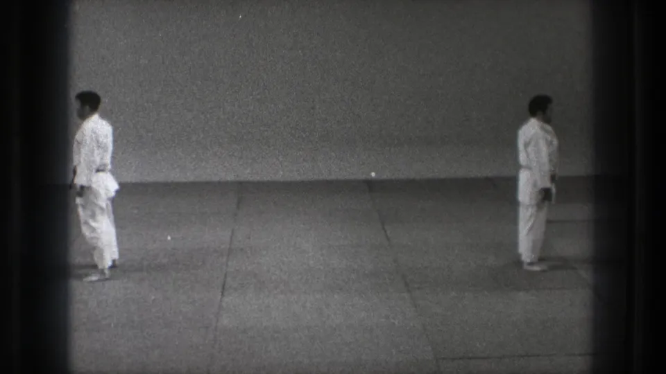 1971 Tokyo 8mm frame showing two karate practitioners in white gi facing each other across a simple mat.