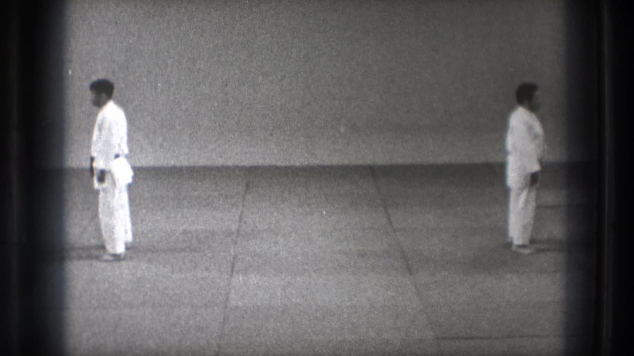 1971 Tokyo 8mm frame showing two men in karate gi standing opposite each other in a restrained practice space.