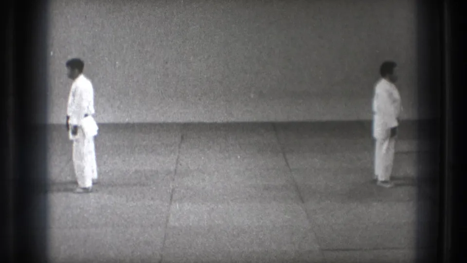1971 Tokyo 8mm frame showing two men in karate gi standing opposite each other in a restrained practice space.