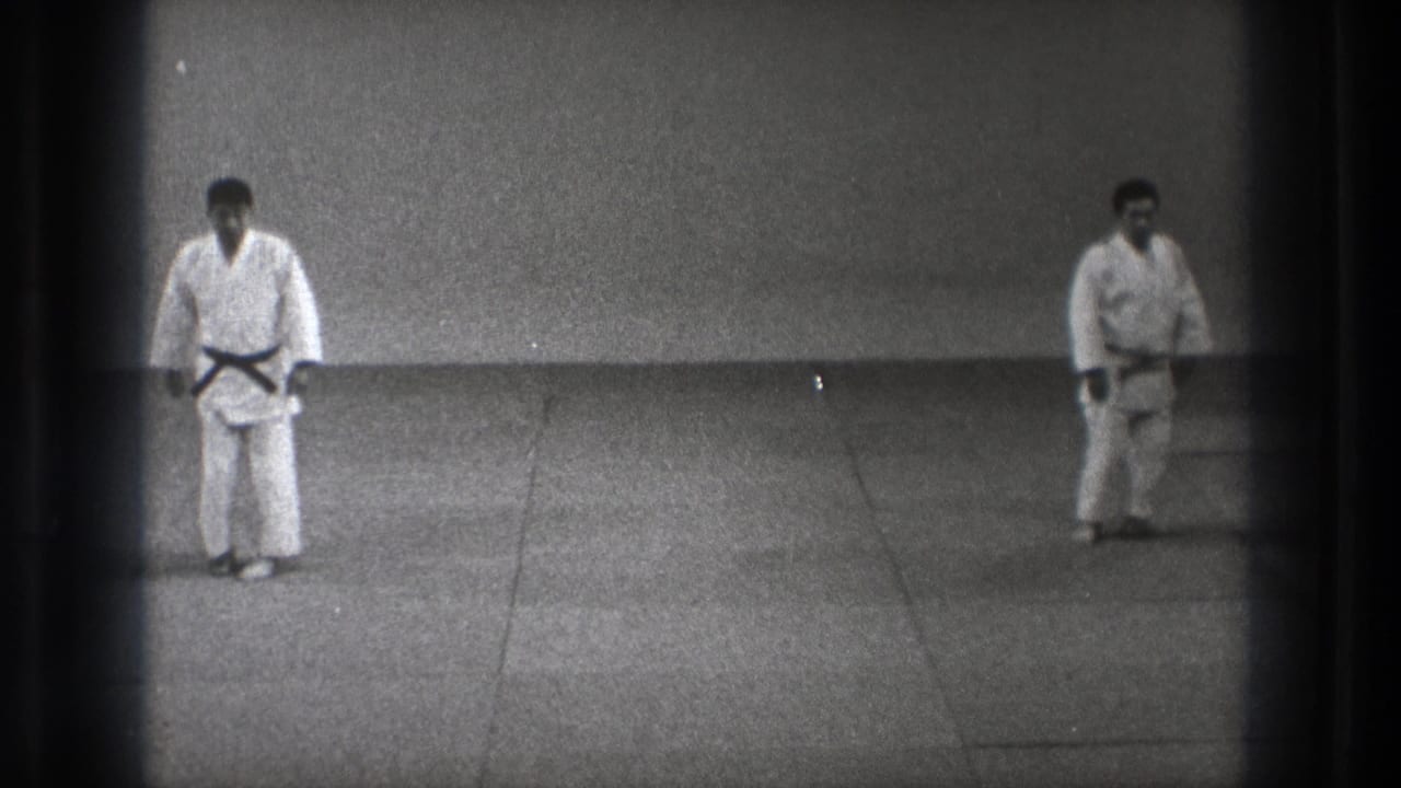 1971 Tokyo 8mm frame showing two adult martial artists in white gi and black belts facing on a plain dojo mat.