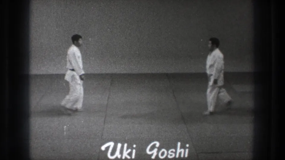 1971 Tokyo 8mm frame showing two gi-clad practitioners stepping toward each other on a dojo mat with 'Uki Goshi' text visible.
