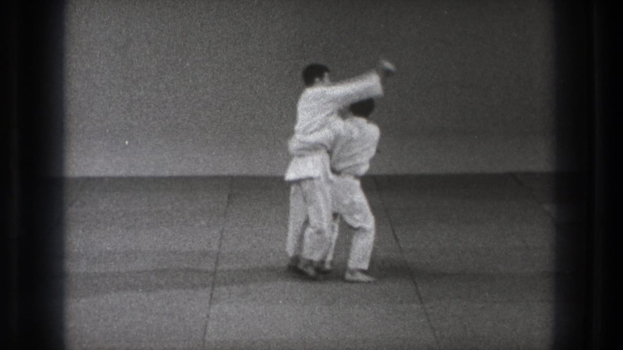 Two men in white judo uniforms begin a grappling throw on a mat.