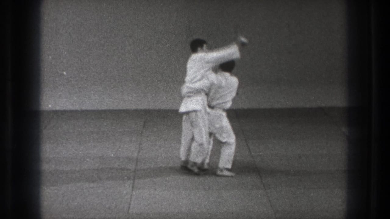 In the Tokyo judo practice scene, one man pivots into a throw while the other stays close at his side.