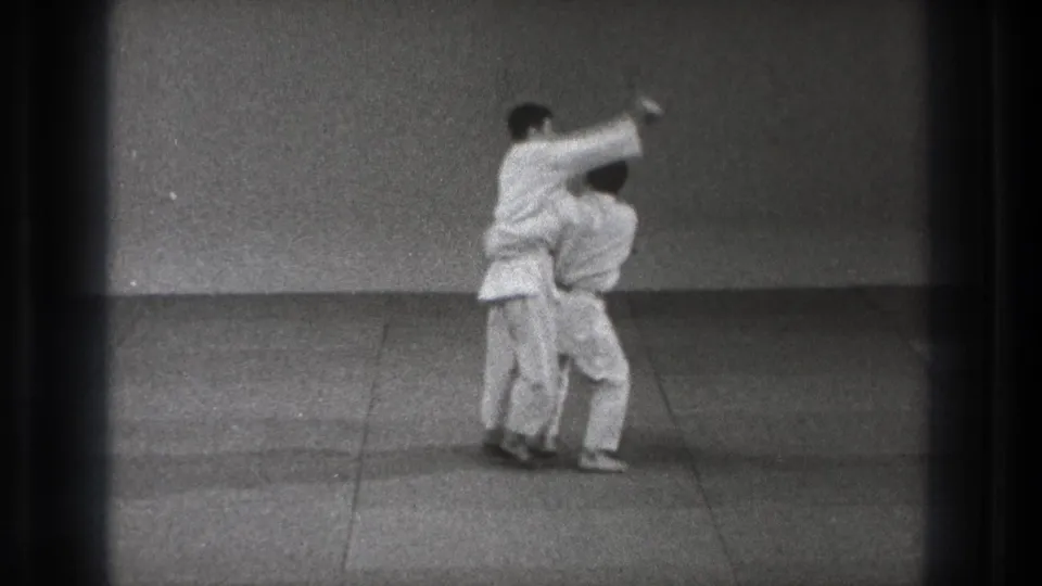 In the Tokyo judo practice scene, one man pivots into a throw while the other stays close at his side.