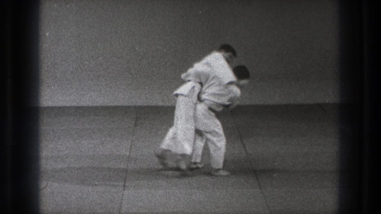 Late in the 1971 Tokyo judo clip, both men remain bent into the grappling technique on the plain practice mat.