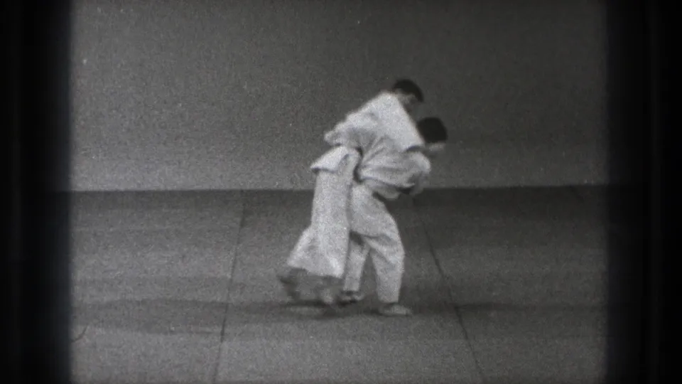 Late in the 1971 Tokyo judo clip, both men remain bent into the grappling technique on the plain practice mat.