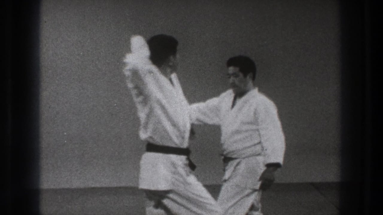 One man raises an arm while the other reaches in during a close martial arts training exchange in 1971 Tokyo footage.