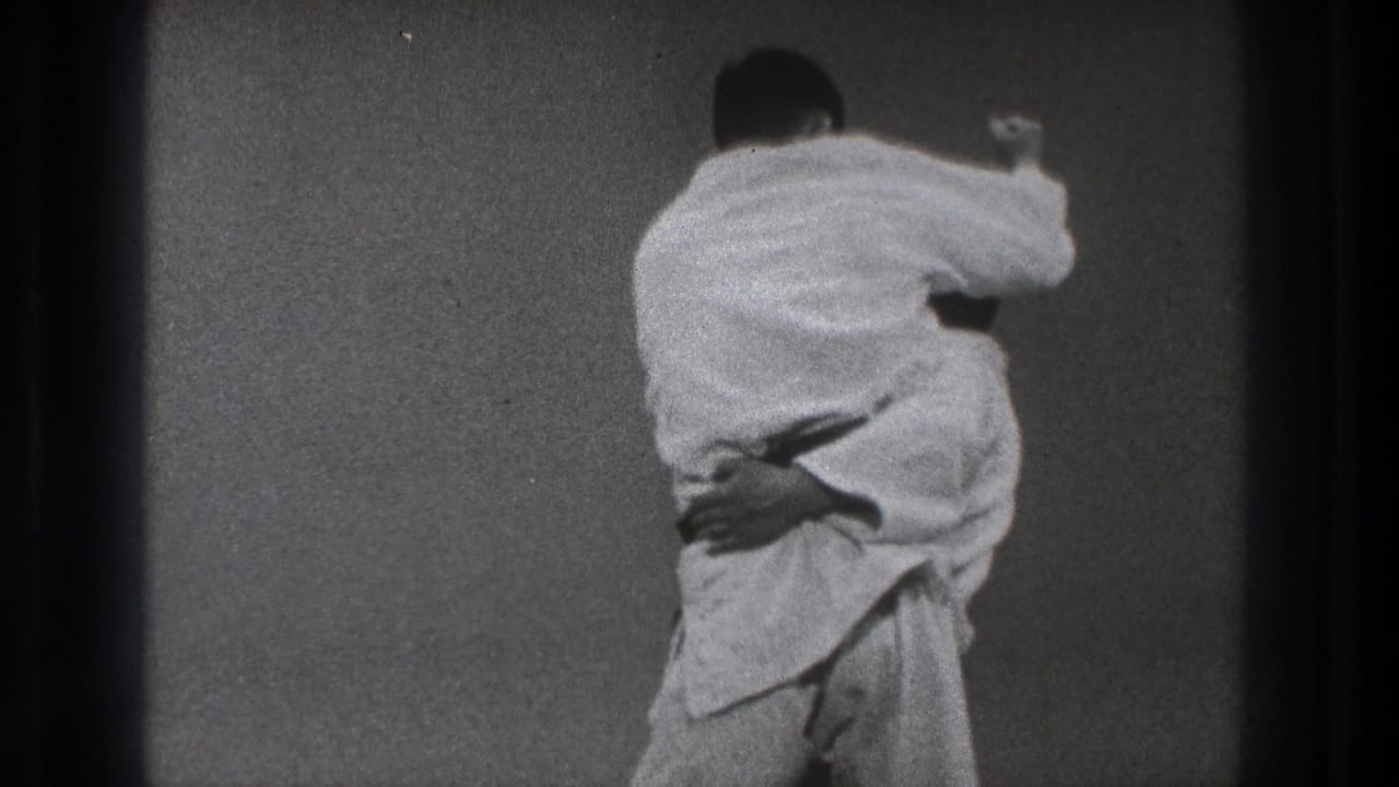 A man in a white gi kneels over or controls his partner on the grey mat after a throw in the Tokyo practice room.