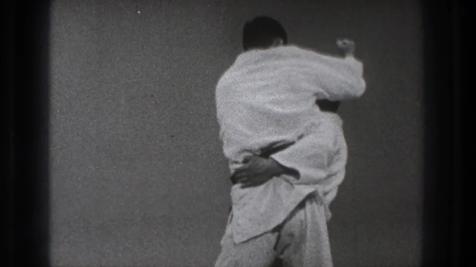 A man in a white gi kneels over or controls his partner on the grey mat after a throw in the Tokyo practice room.