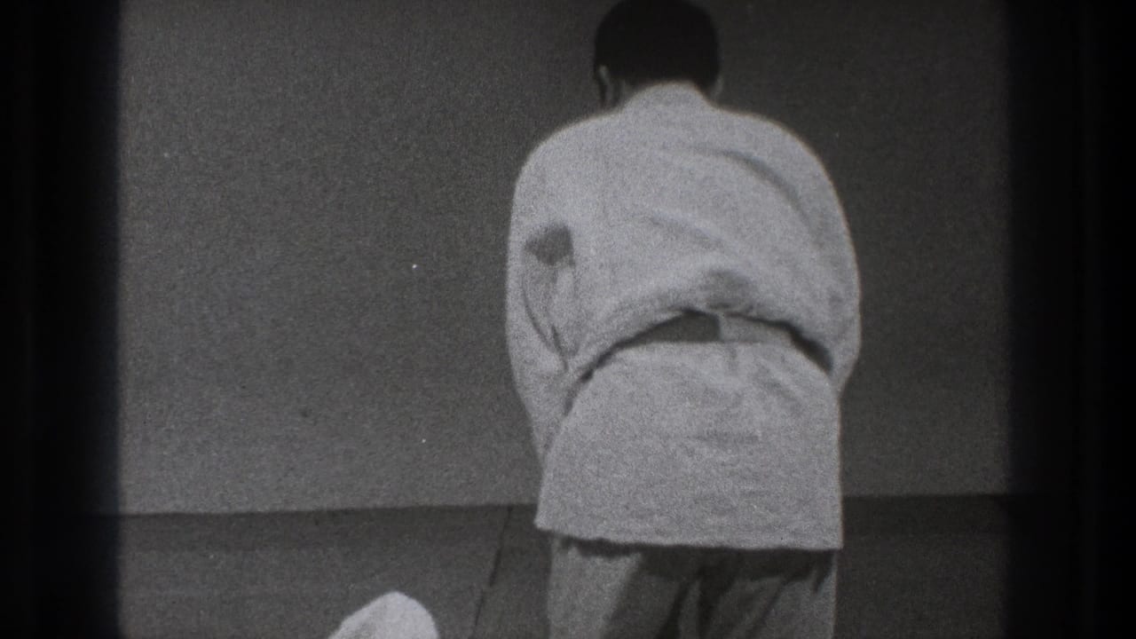 A man in a white gi stands with his back to the camera on the mat, following the completed throw in the Tokyo practice sequence.