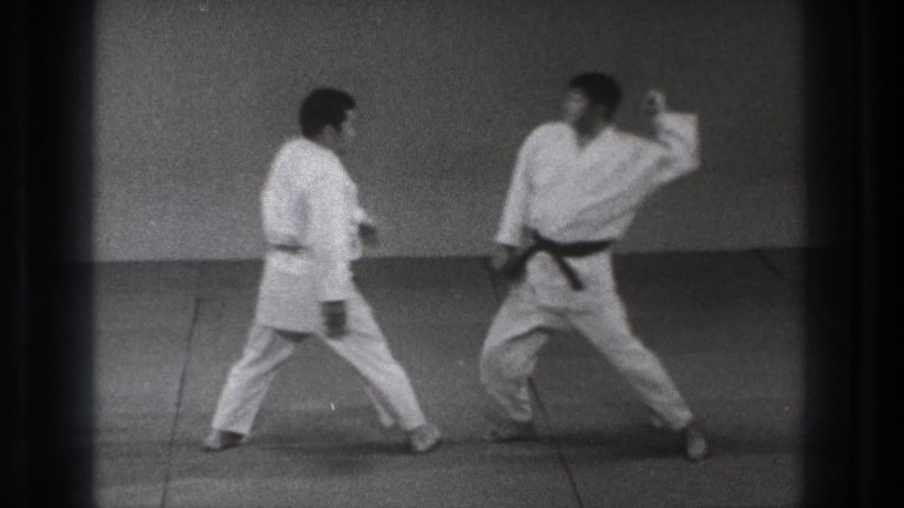 Two martial arts practitioners in gi close distance on the mat, with one extending an arm during the technique.