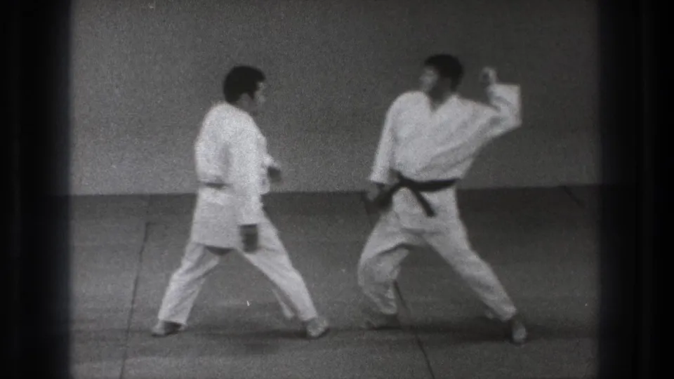 Two martial arts practitioners in gi close distance on the mat, with one extending an arm during the technique.