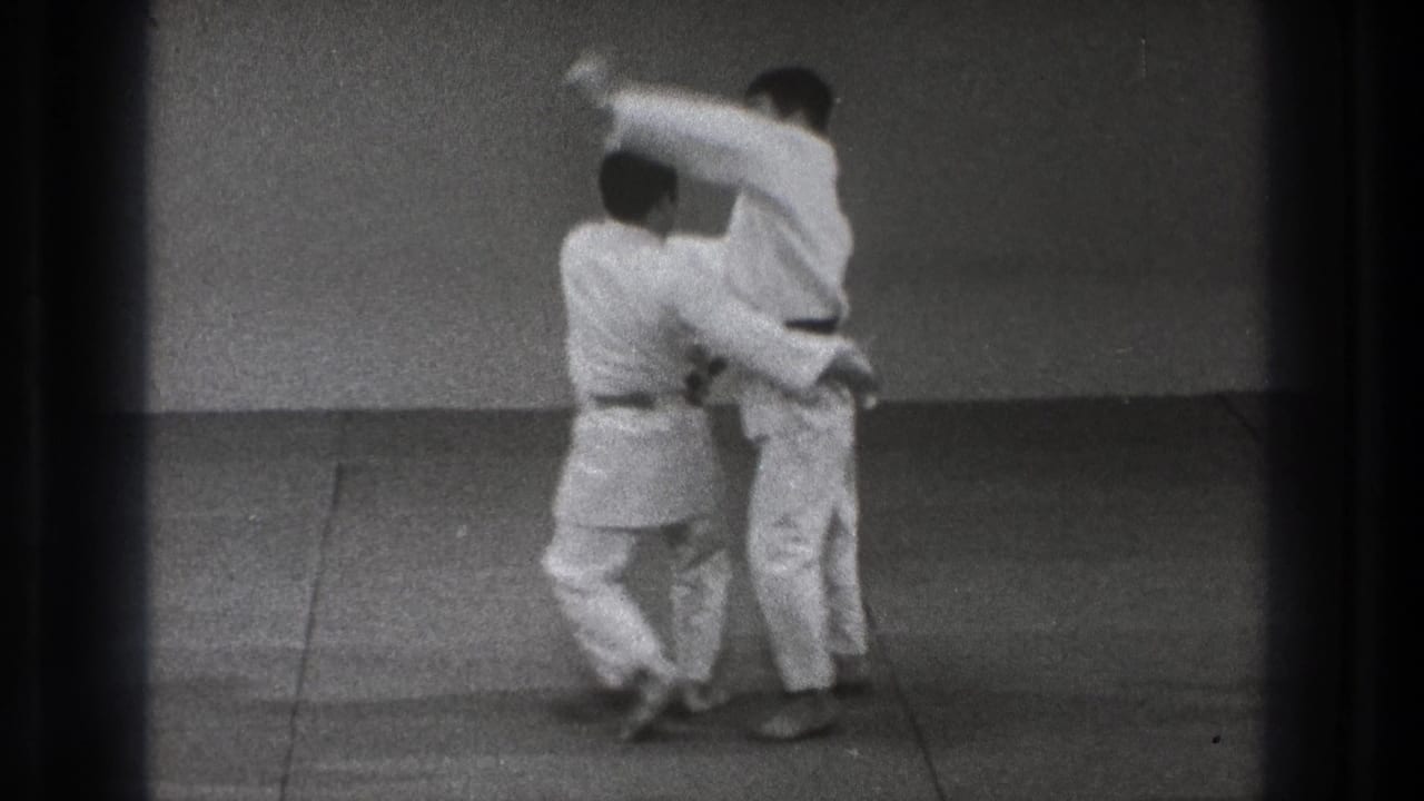 A close-contact technique is underway as one man in a gi lifts or turns his partner on the dojo mat.