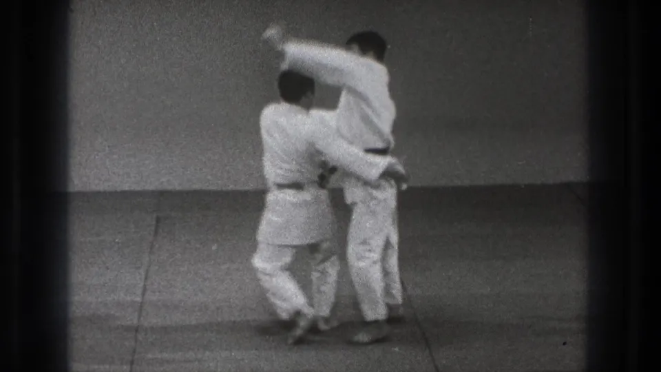 A close-contact technique is underway as one man in a gi lifts or turns his partner on the dojo mat.
