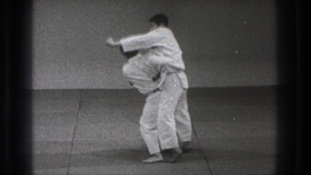 Two men in white martial arts uniforms begin a grappling exchange on a mat.