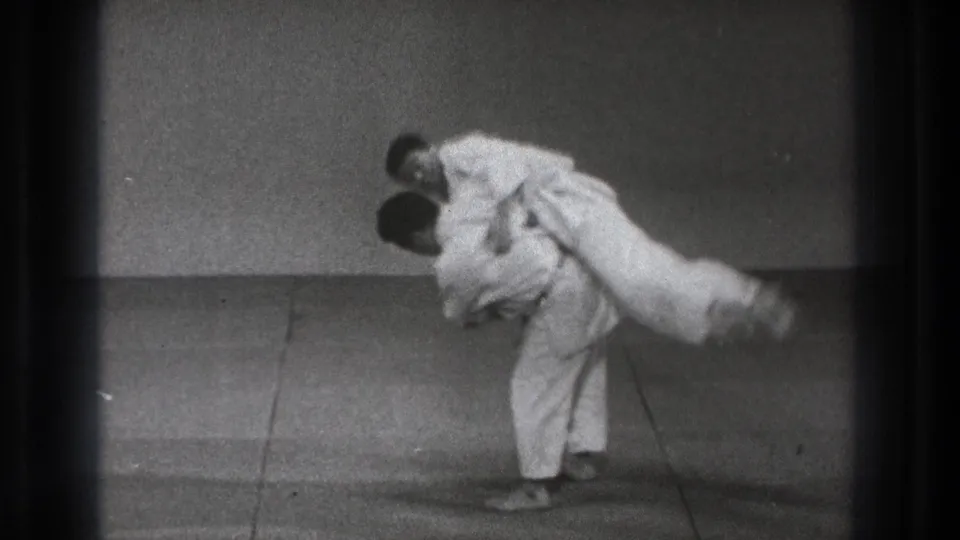 A 1971 Tokyo martial arts practice frame shows one man lifting his opponent across the hip on a simple mat.