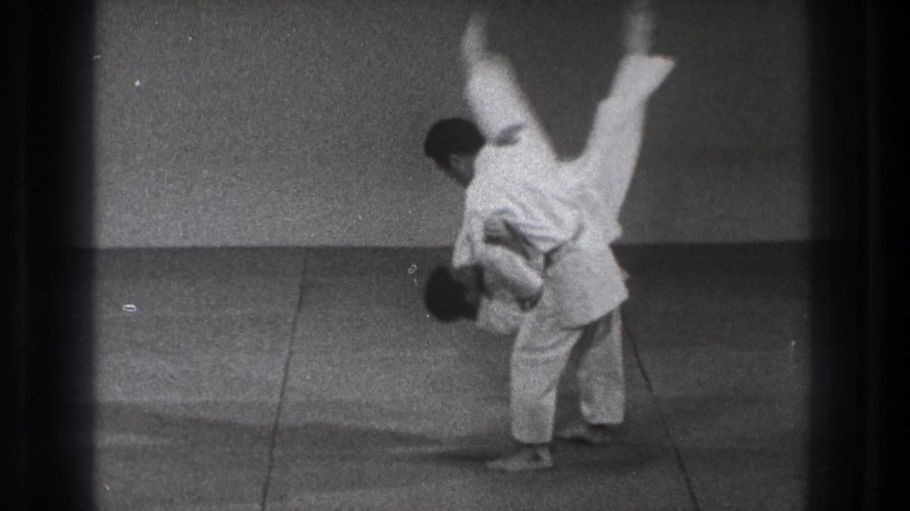 The martial arts throw reaches its peak, with one adult man inverted above the mat in this 1971 Tokyo home-movie frame.