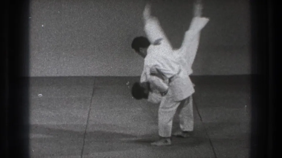 The martial arts throw reaches its peak, with one adult man inverted above the mat in this 1971 Tokyo home-movie frame.