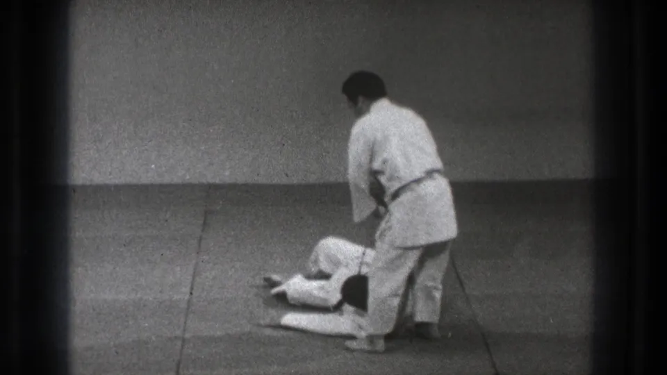 In 1971 Tokyo footage, two adult men practice martial arts on a tatami mat as one stands over the other after a floor technique.