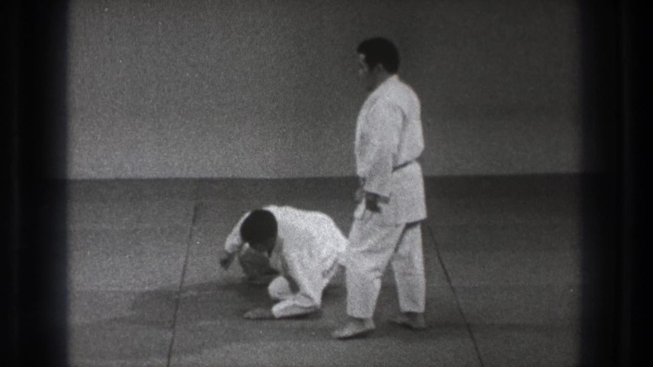 The 1971 Tokyo training scene shows one practitioner down on the mat while his partner stands close by in a white gi.
