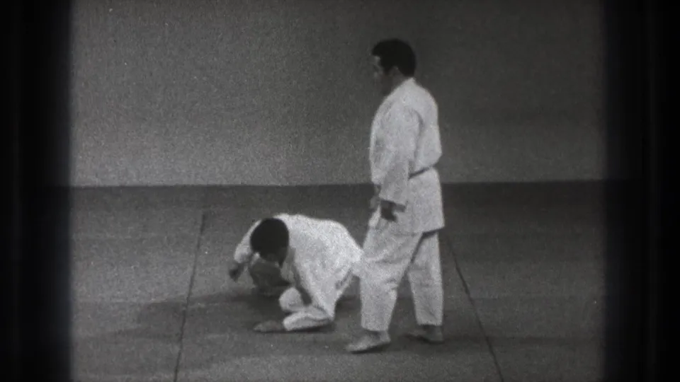The 1971 Tokyo training scene shows one practitioner down on the mat while his partner stands close by in a white gi.