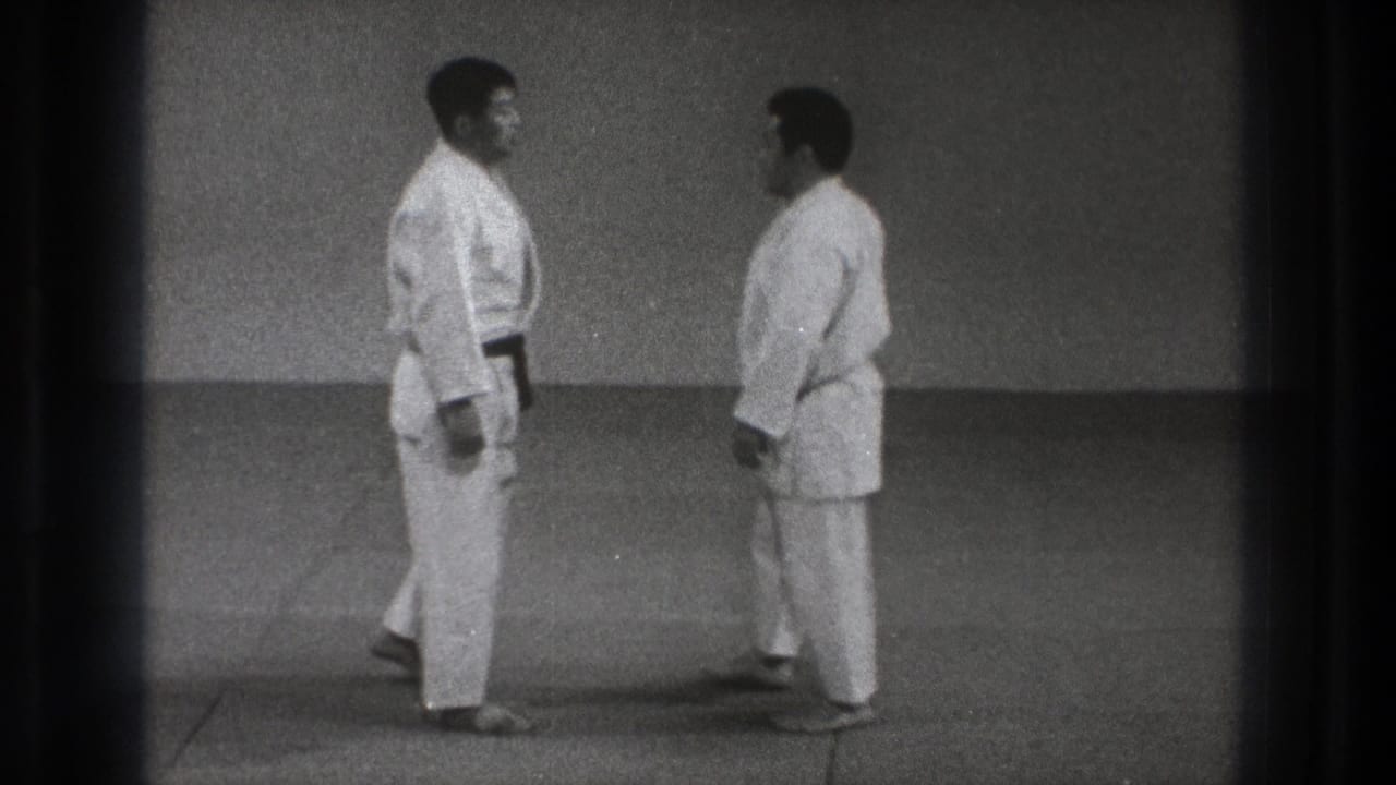 In 1971 Tokyo home-movie footage, two adult martial arts practitioners in white gi face each other before a demonstration.