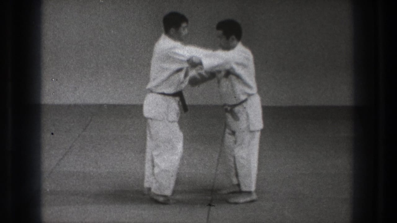 Two martial artists in white gi grip each other on a mat.