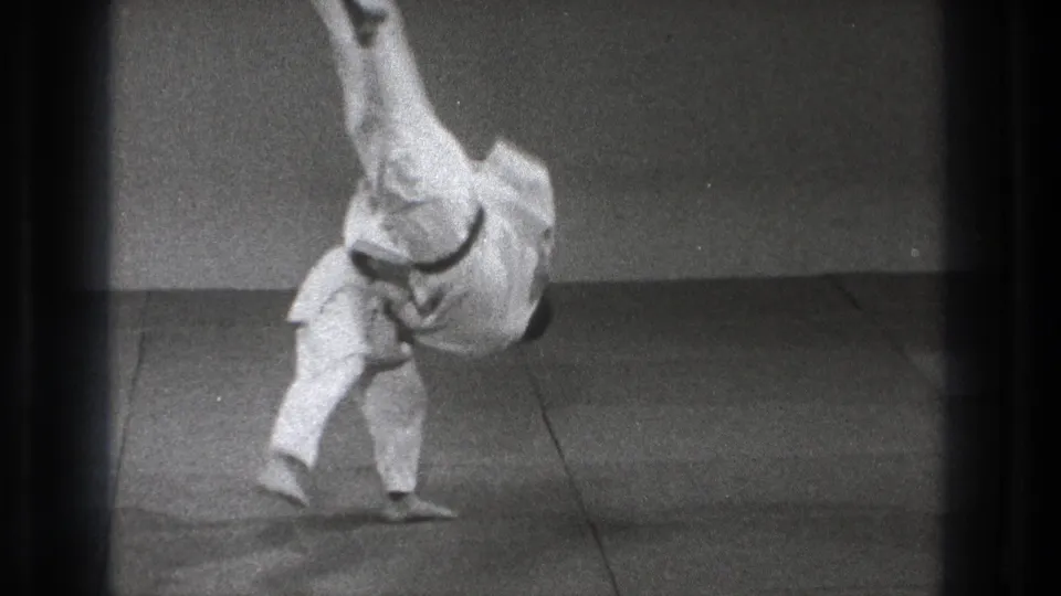 Tokyo 1971 frame of a karate practitioner completing a dynamic throw, with one leg elevated and an arm near the indoor mat for balance.