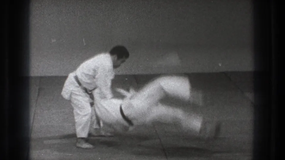 In 1971 Tokyo footage, a man in a white gi appears to execute a throw or handstand kick with a training partner on a mat.
