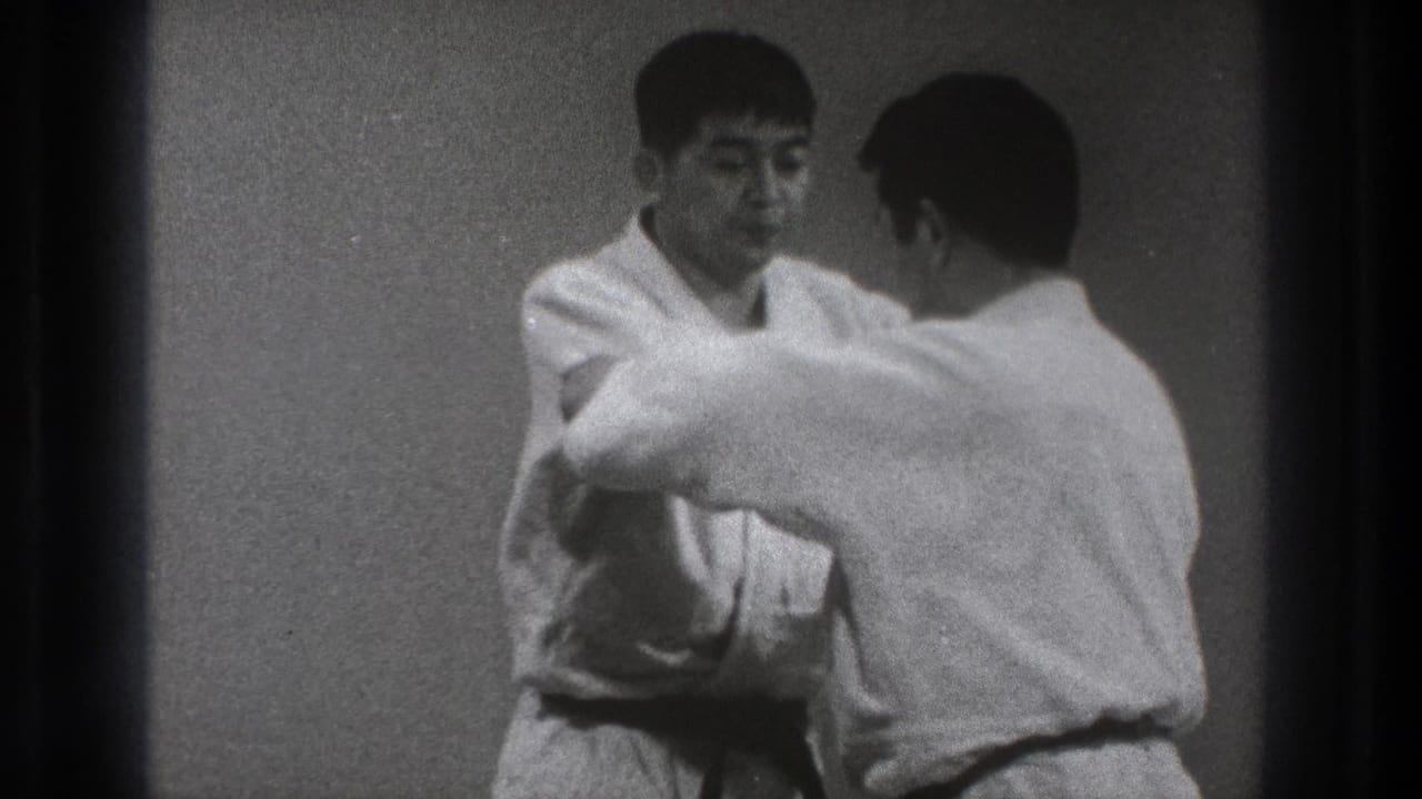 Two adult men in white gi practice close-quarters karate technique in a plain Tokyo dojo setting, based on supplied 1971 metadata.