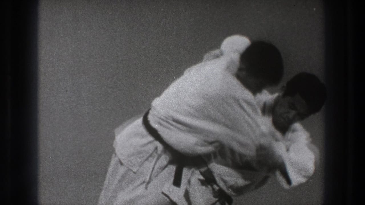 Two men in white gi grapple on a mat during martial arts practice.