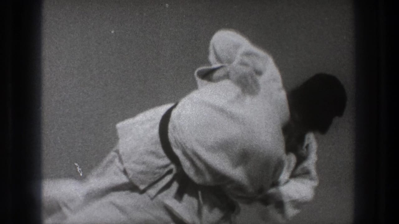 The black-and-white 8mm frame shows two adult men in gi low on the mat during a continued judo-style technique.