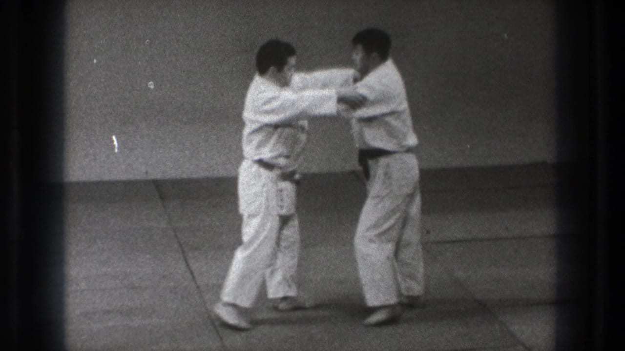 Two men in karate gi face each other on an indoor mat.