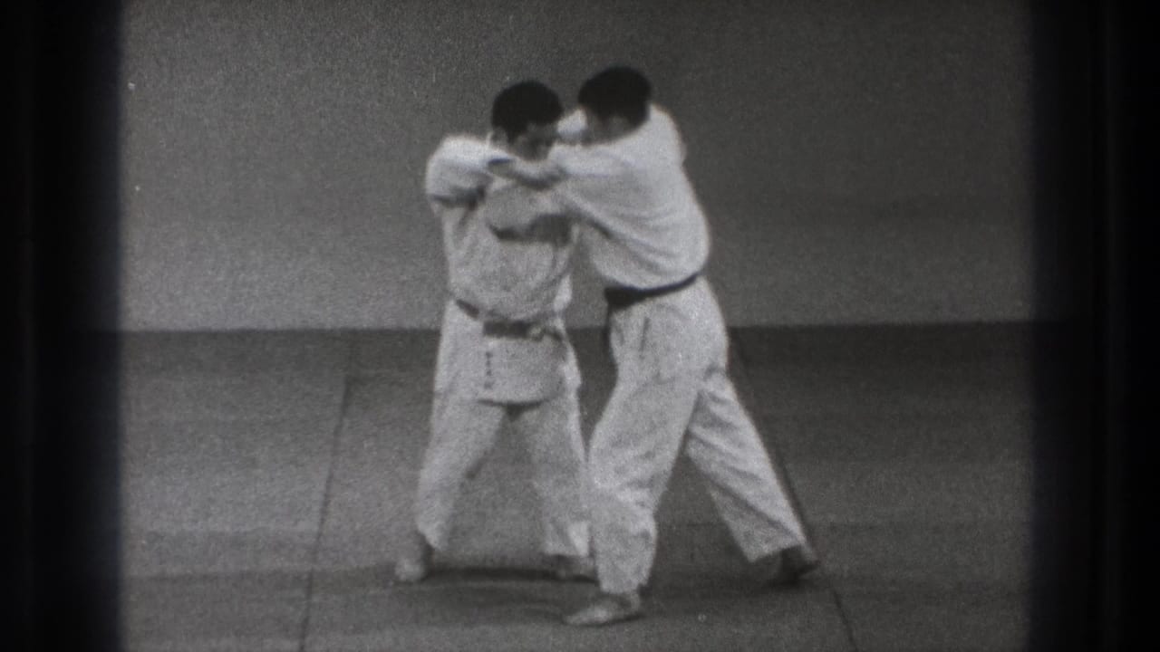 The karate drill continues as one man pivots or bends while the other maintains close control in the indoor Tokyo practice scene.