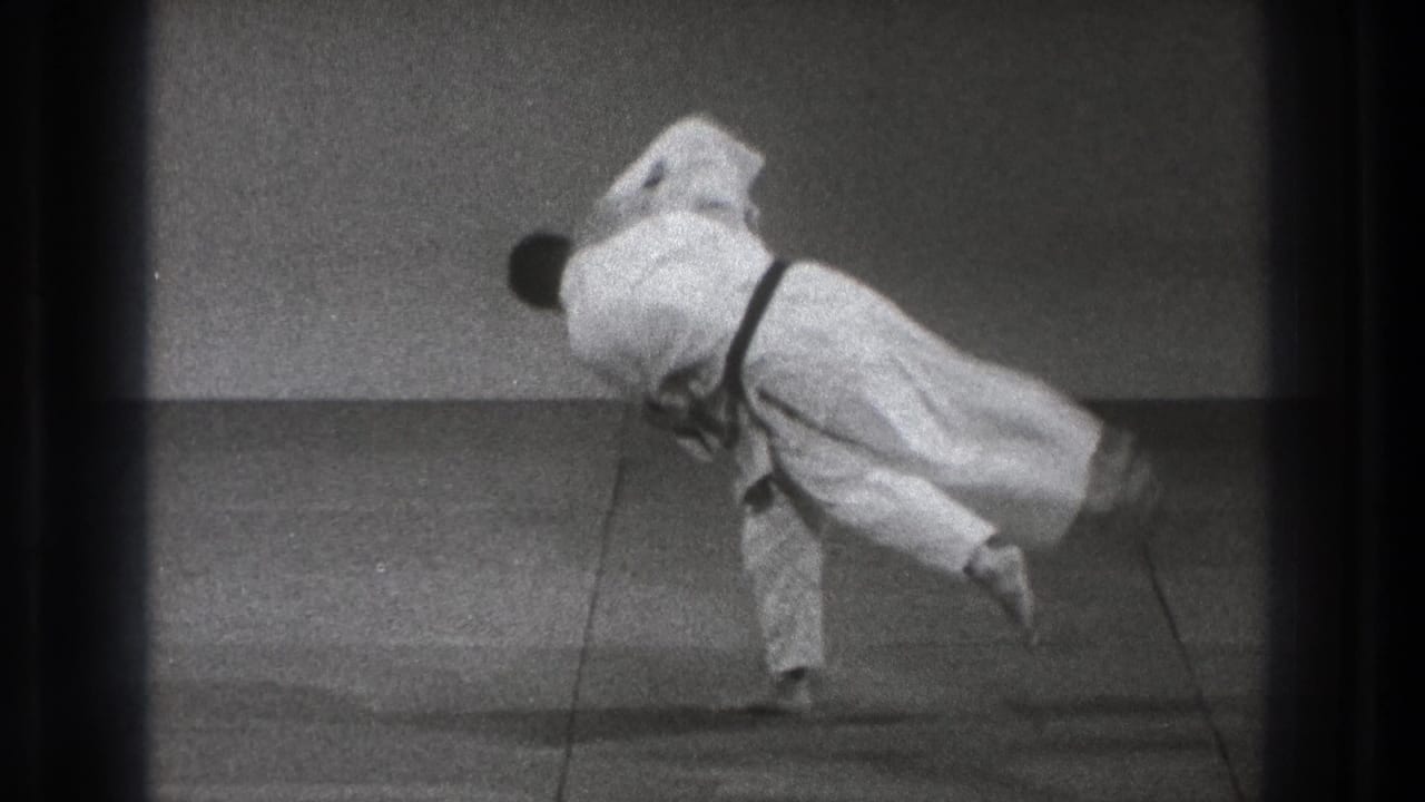 One practitioner is carried sideways through the throw, with both white gi blurred by the fast motion in the black-and-white 8mm frame.