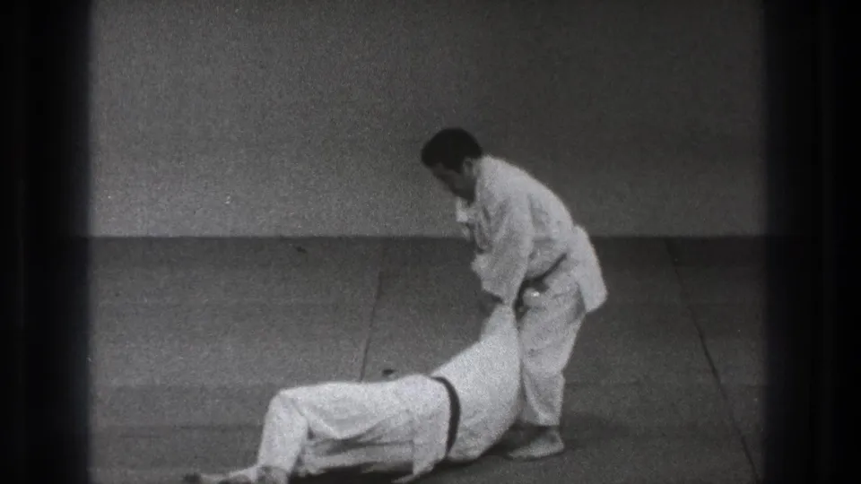 In the 1971 Tokyo martial arts demonstration, one man stands over a partner who has been taken down on the mat.