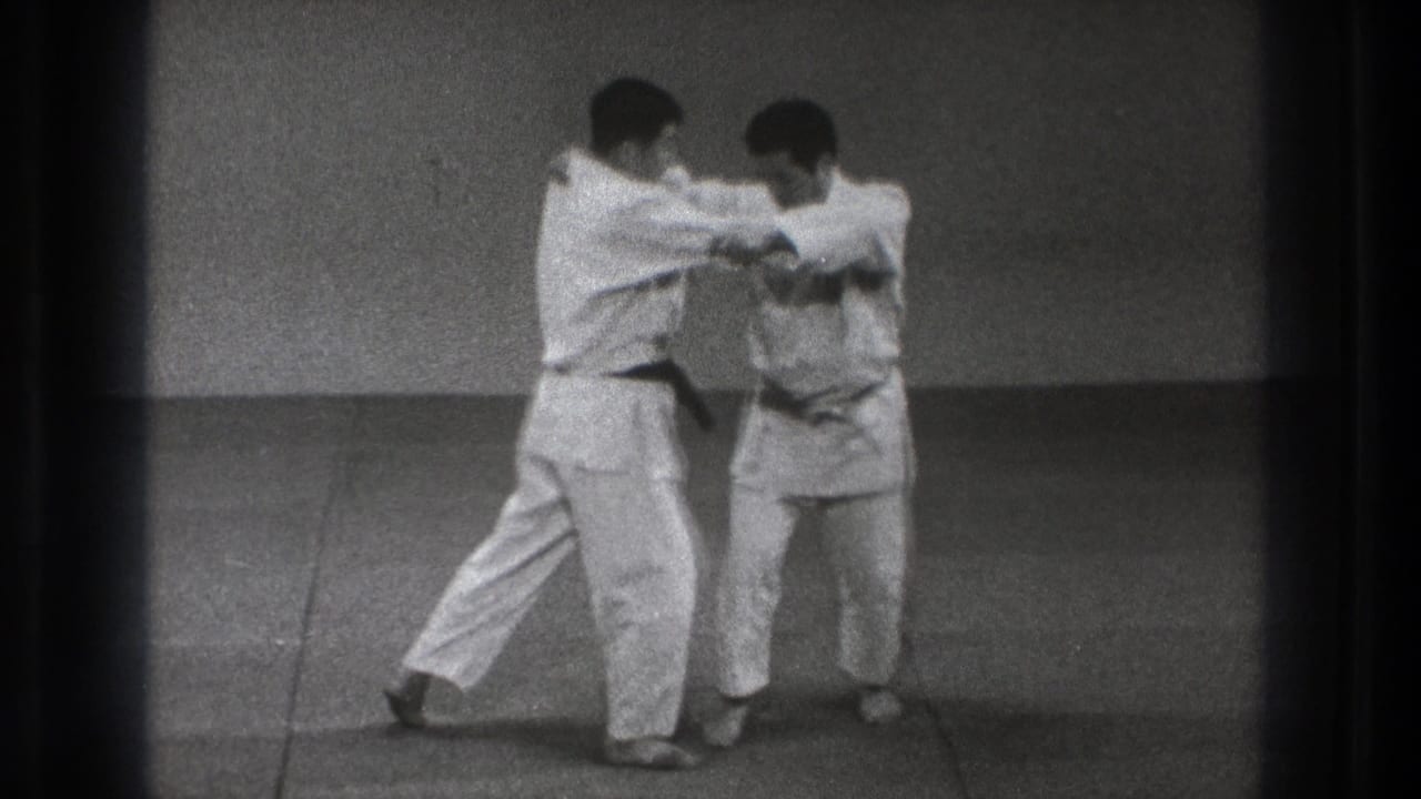 The 1971 Tokyo dojo scene shows two adult martial artists maintaining sleeve and lapel control before the throw develops.