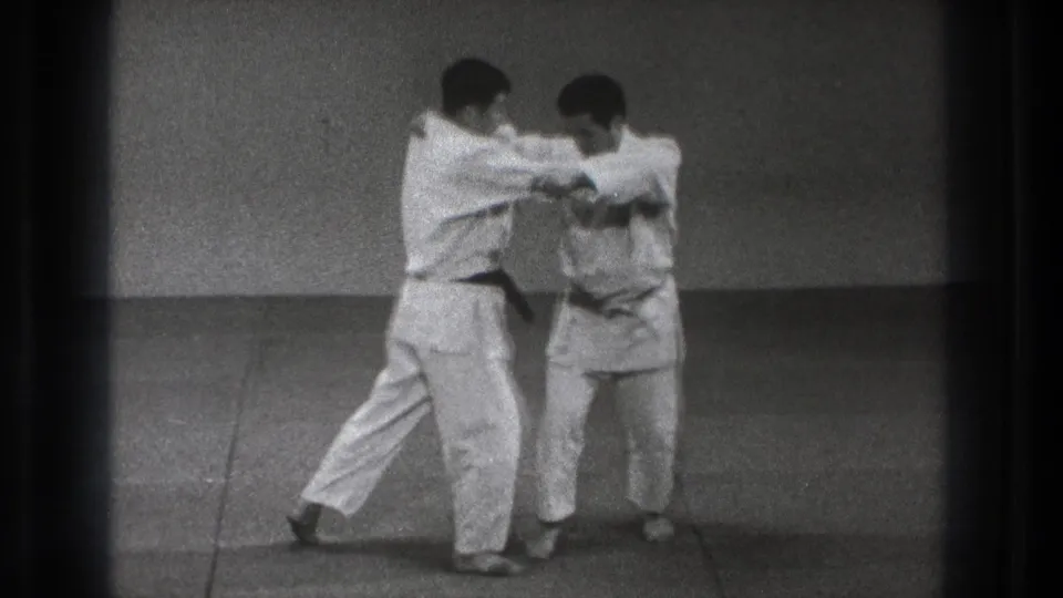 The 1971 Tokyo dojo scene shows two adult martial artists maintaining sleeve and lapel control before the throw develops.