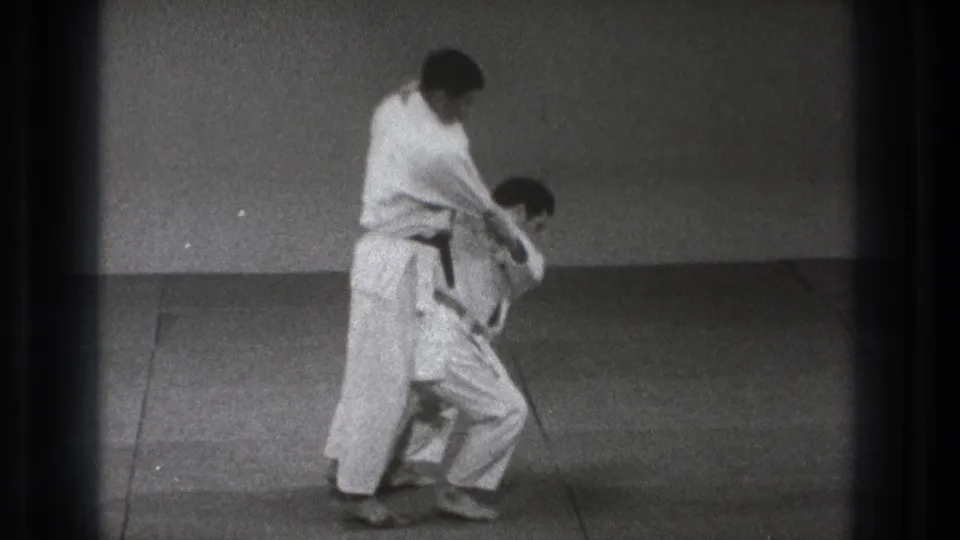 One adult practitioner turns his body in front of the other during the 1971 Tokyo Turikomi Goshi demonstration, preparing the hip throw.