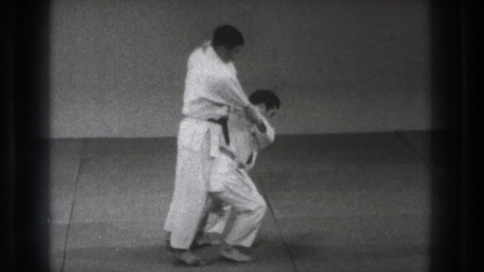In Tokyo, Japan, 1971, two men in white gi practice a karate throw on a simple indoor mat.